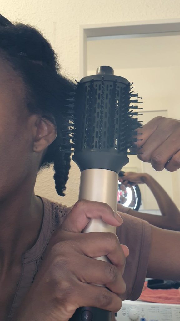 Utilisation d’une brosse soufflante cheveux crépus pour étirer une mèche lors du séchage